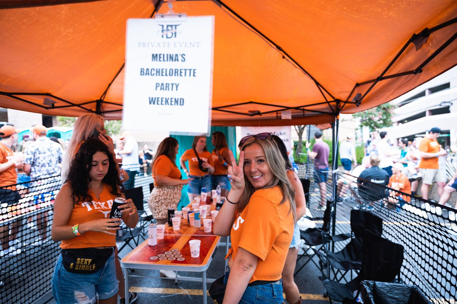 Outdoor party scene with orange tent and bachelorette party sign visible.