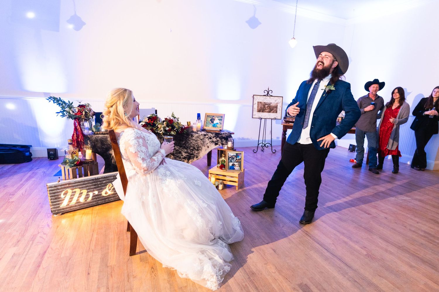 A wedding couple performs a playful dance routine on a wooden floor with blue ambient lighting.