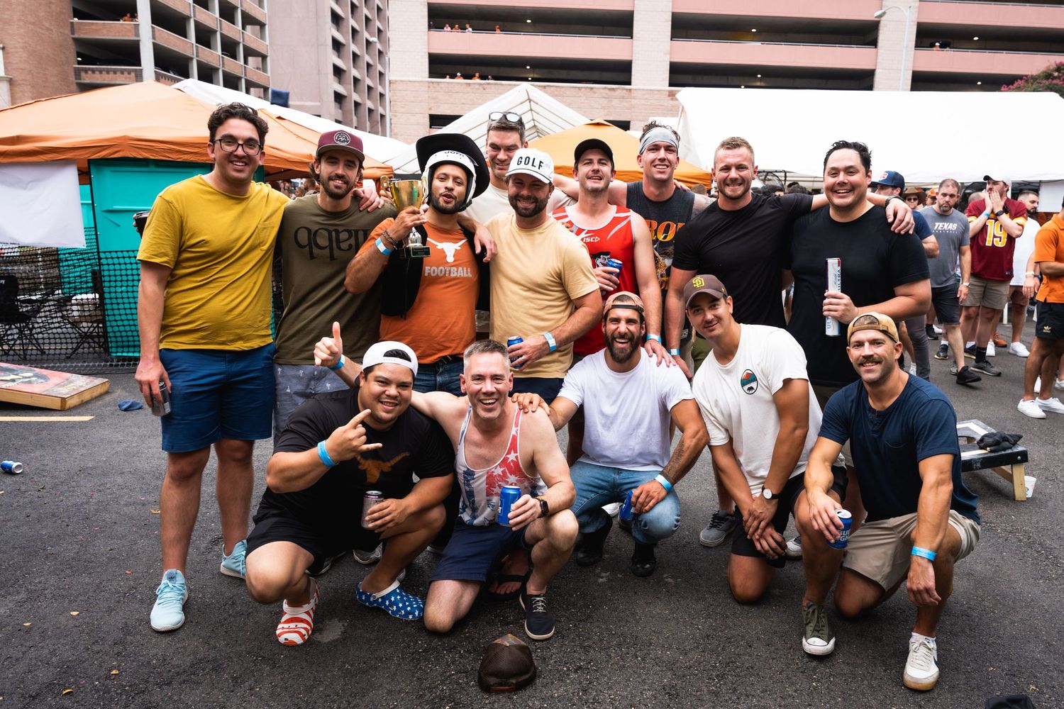 A group of sports fans pose together for a photo in front of portable toilets at a tailgate event.