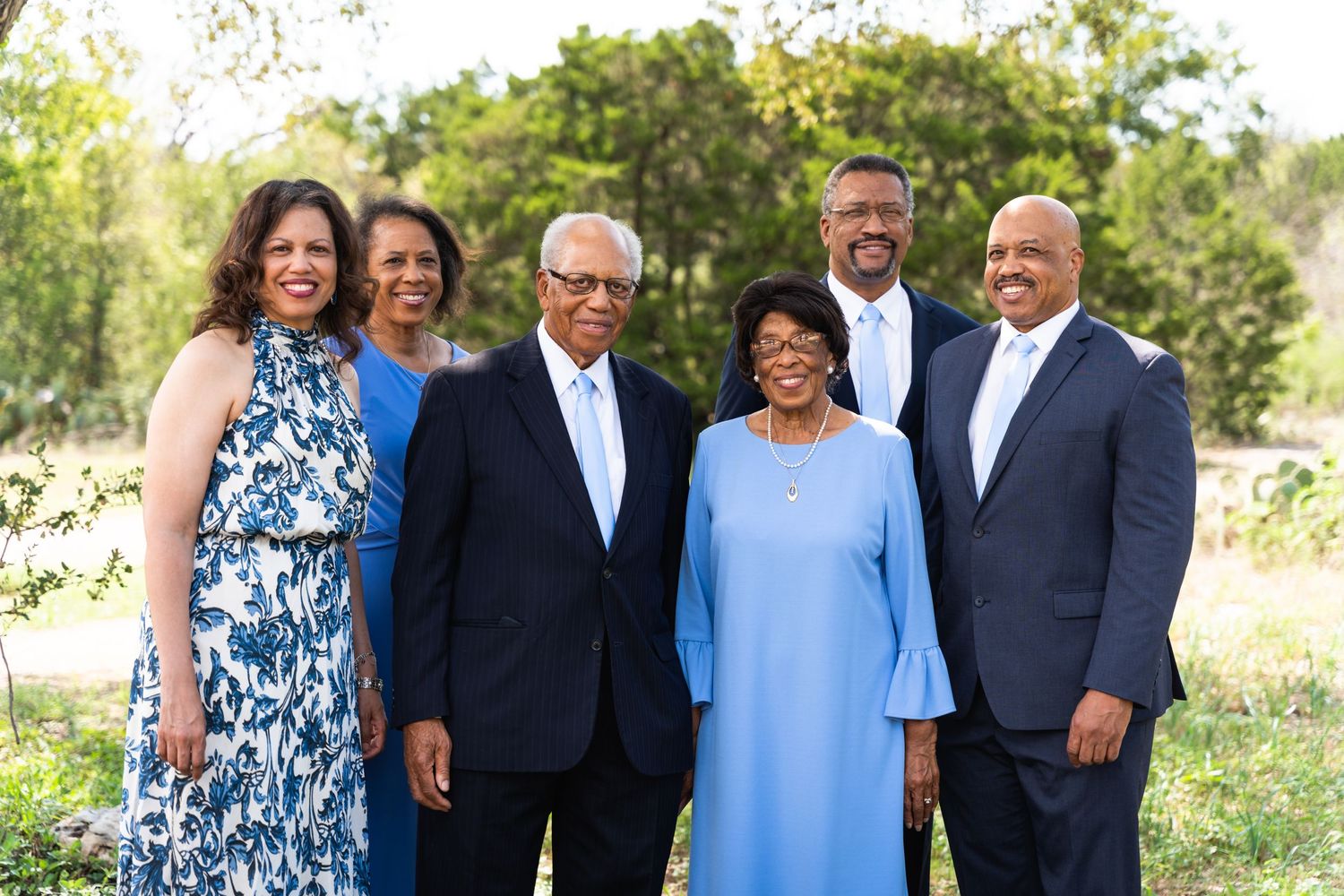 A small group poses together outdoors wearing formal attire in blue and white tones.