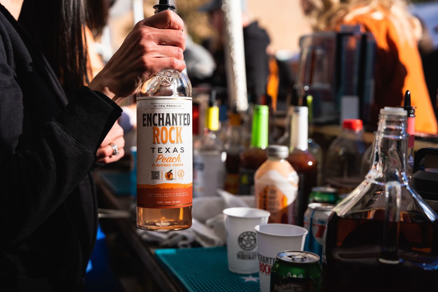 Person holding a bottle of bourbon at a bar station with assorted spirits and mixers.