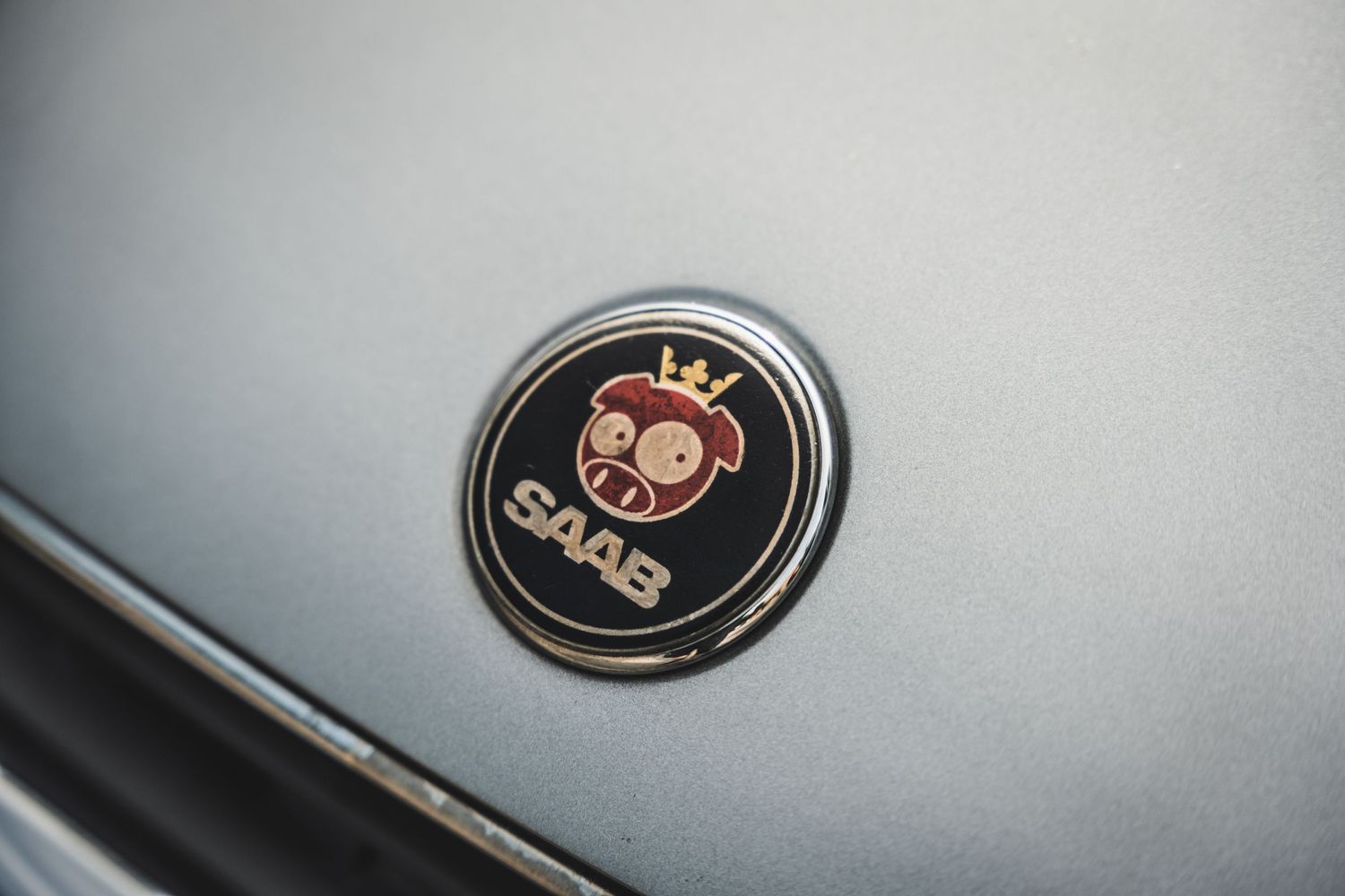 Close-up shot of a vintage Saab emblem badge on a gray metallic surface.