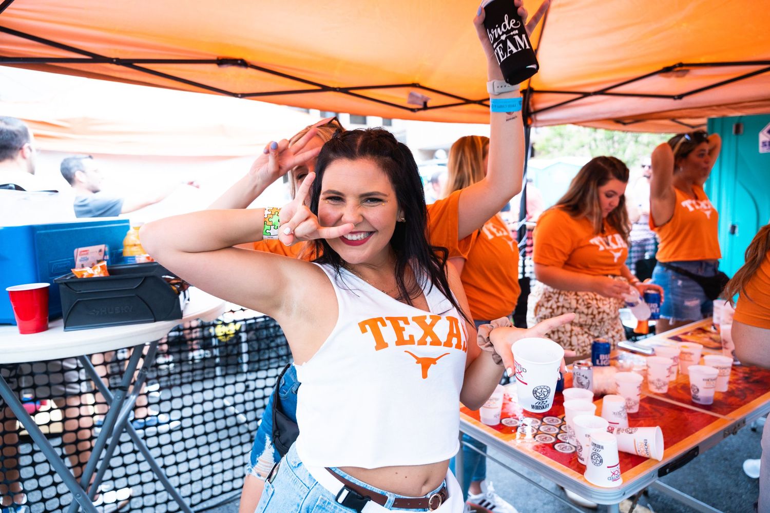 People enjoying a lively celebration under orange tent with drinks and cheering.