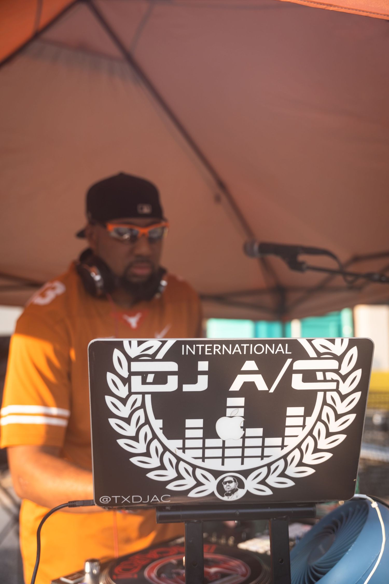 A DJ setup with a laptop displaying the DJ A/C logo under an orange tent.