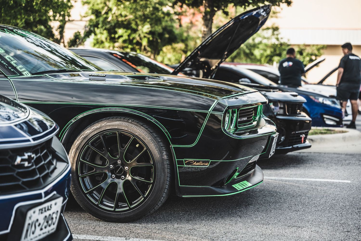 Modified black muscle car with custom wheels and green accents at car show.