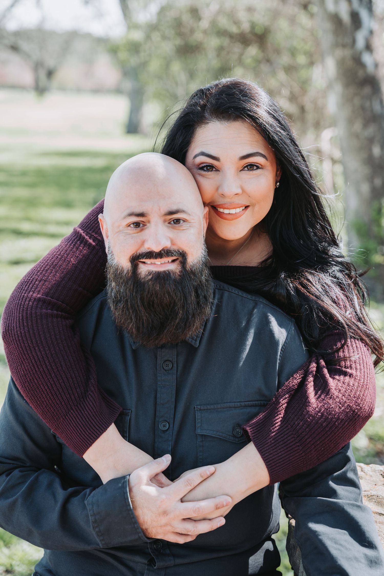 Loving couple embracing outdoors with one wearing burgundy and the other in black.
