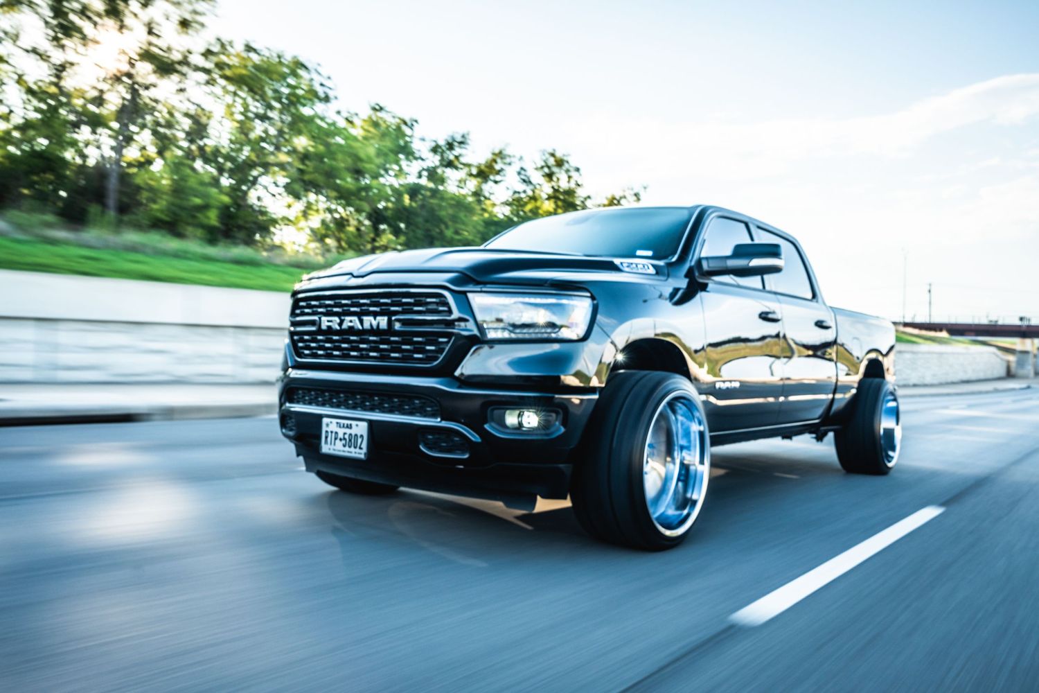 Custom black RAM pickup with chrome wheels photographed in dynamic rolling shot.