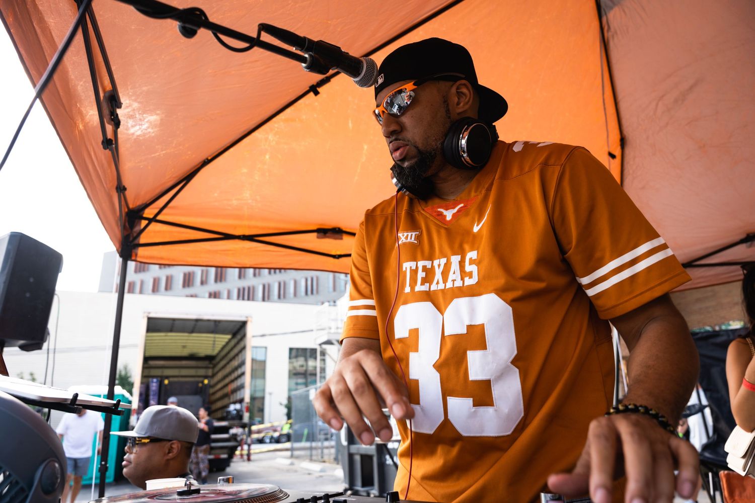 DJ in orange Texas jersey performing at outdoor event.