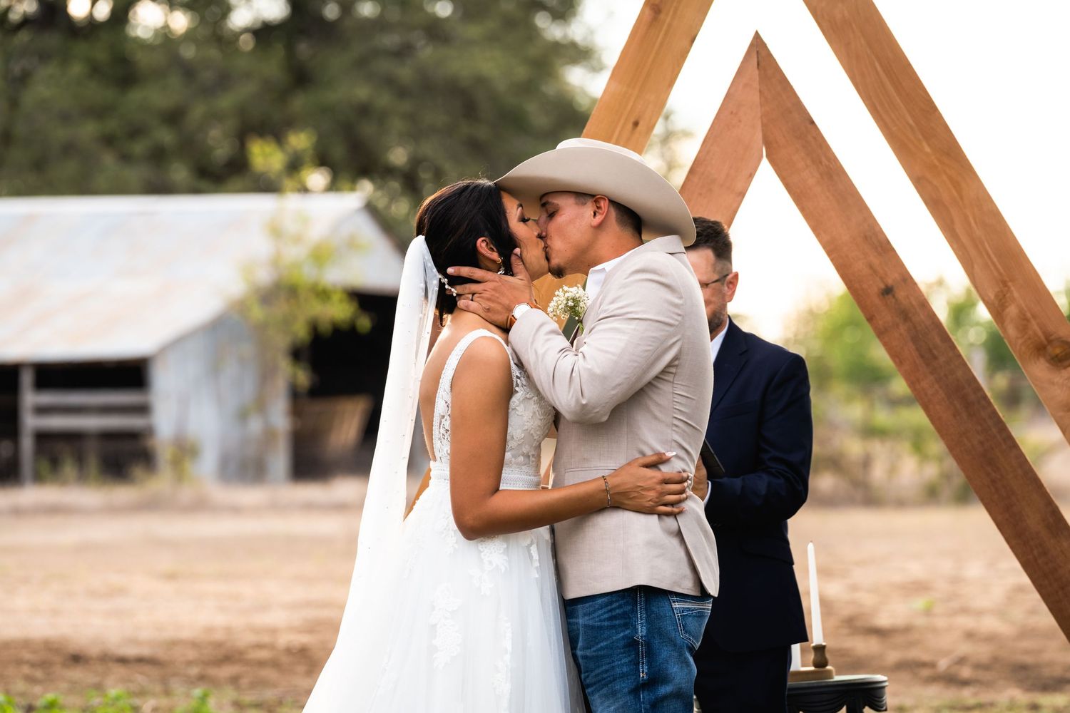 A couple shares their first kiss during wedding ceremony under wooden arch.