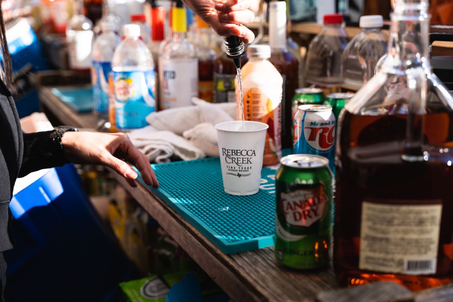 Close-up of a bar setup with various spirits and mixers on a blue rubber mat.