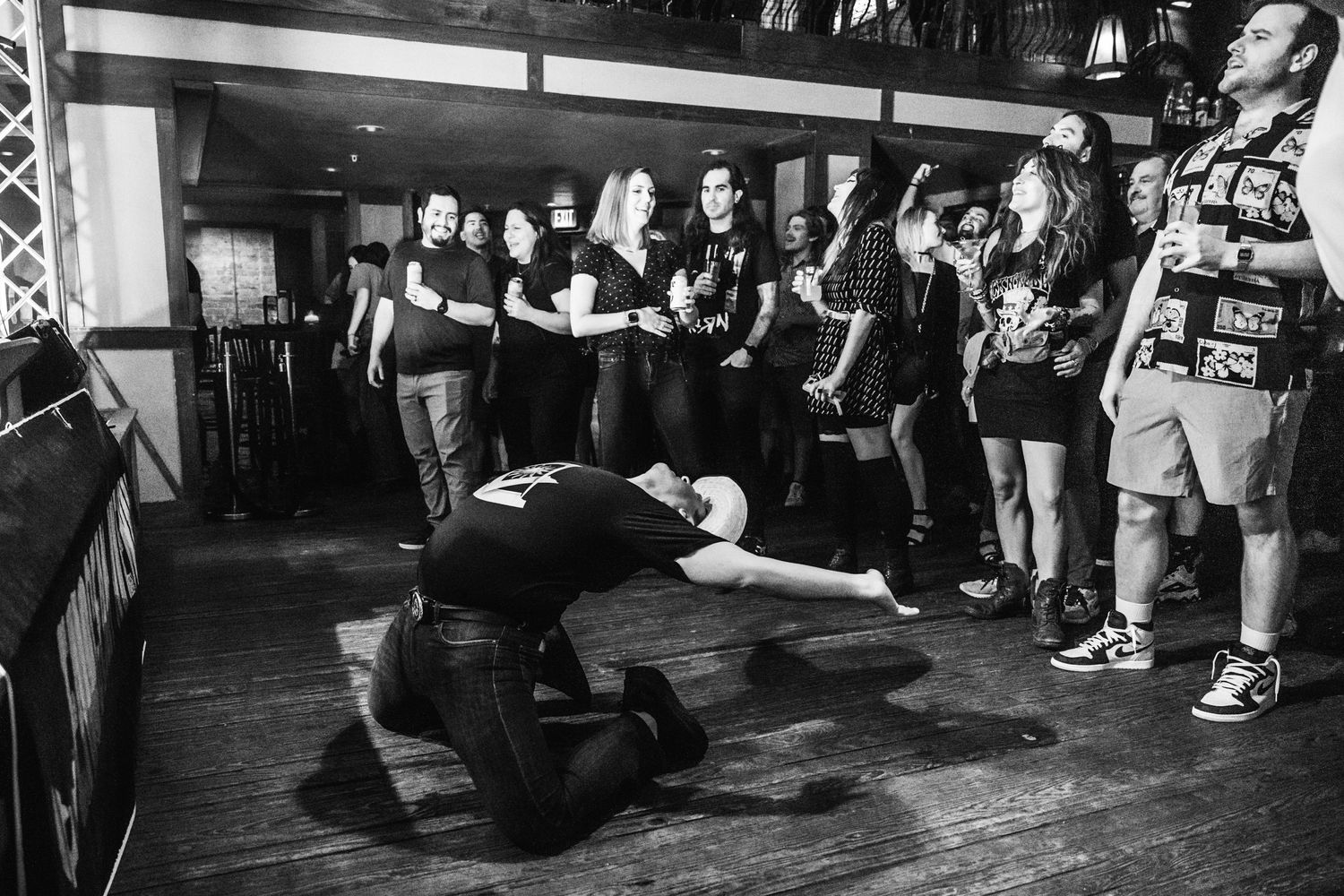 Black and white photo of performer kneeling on stage with crowd watching.