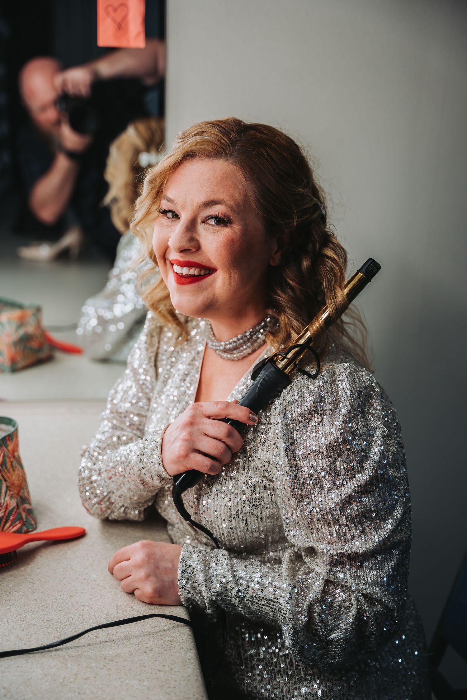 Performer in a glittering silver dress smiling while holding a styling tool.