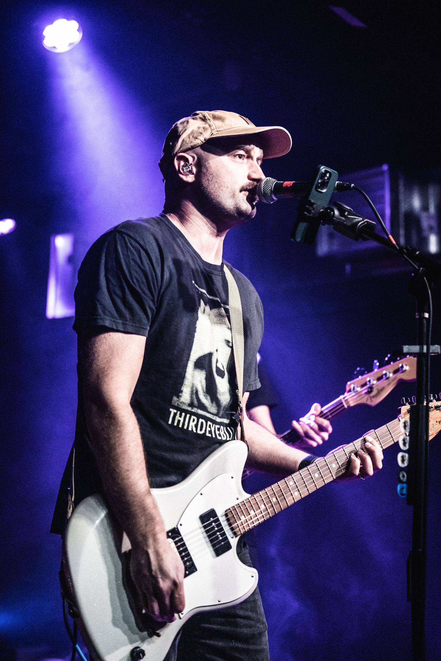 Musician performs with white electric guitar under blue spotlight on concert stage.
