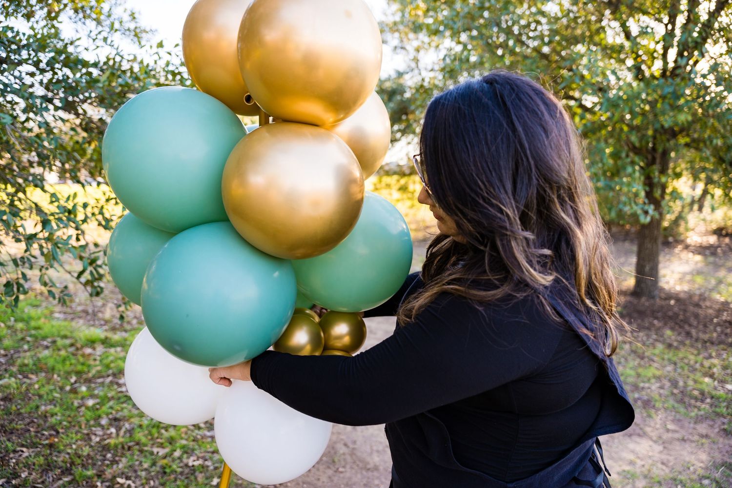 Balloon arch installation combining gold, mint green and white balloons in outdoor setting.
