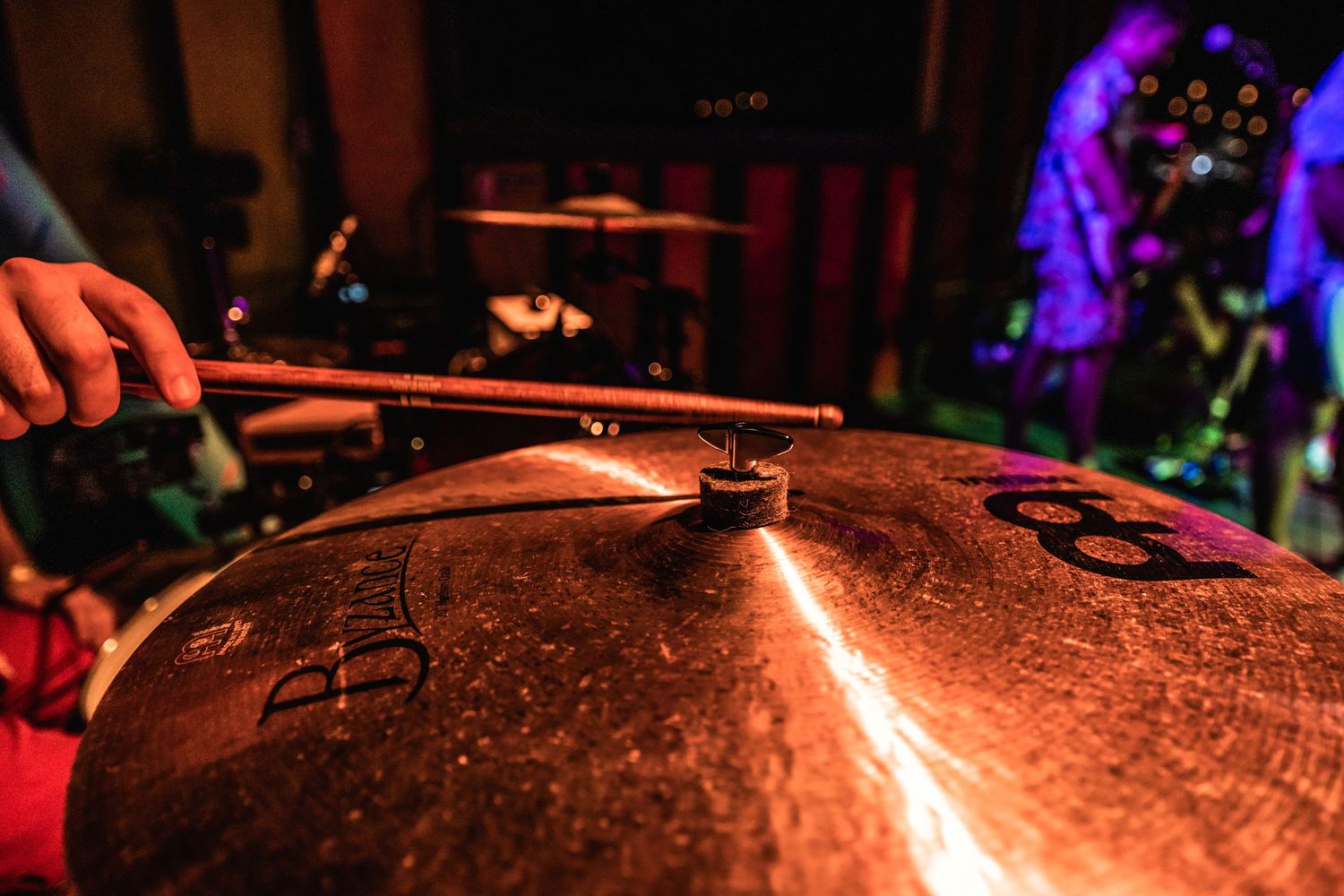 Close-up of drum cymbal with hands playing in dark concert lighting.