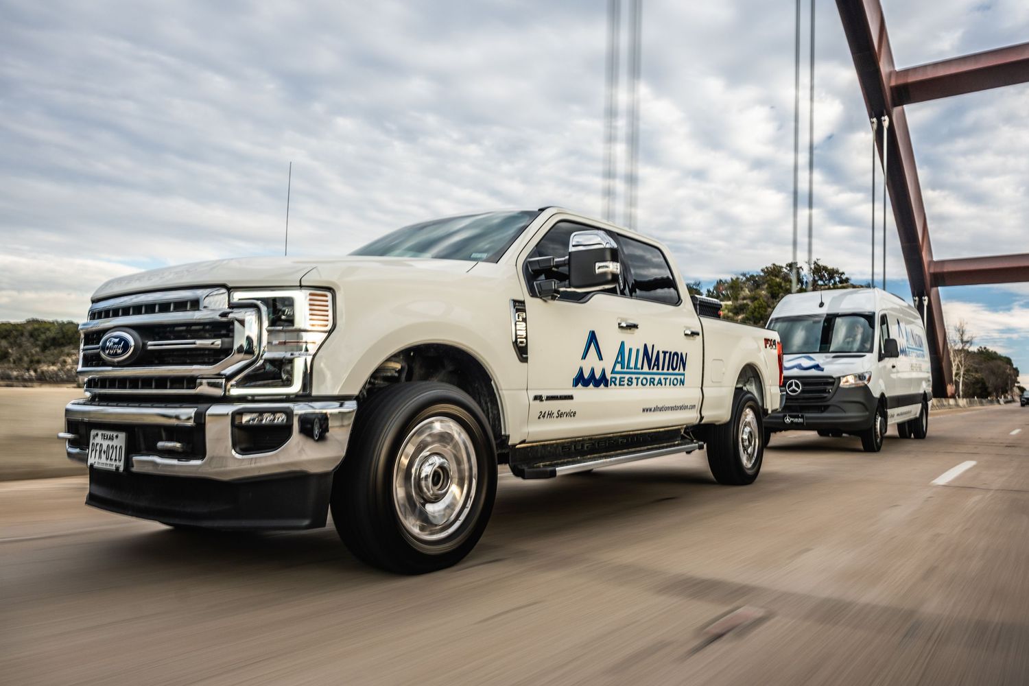 AirNow branded Ford trucks driving across a steel bridge during daytime.