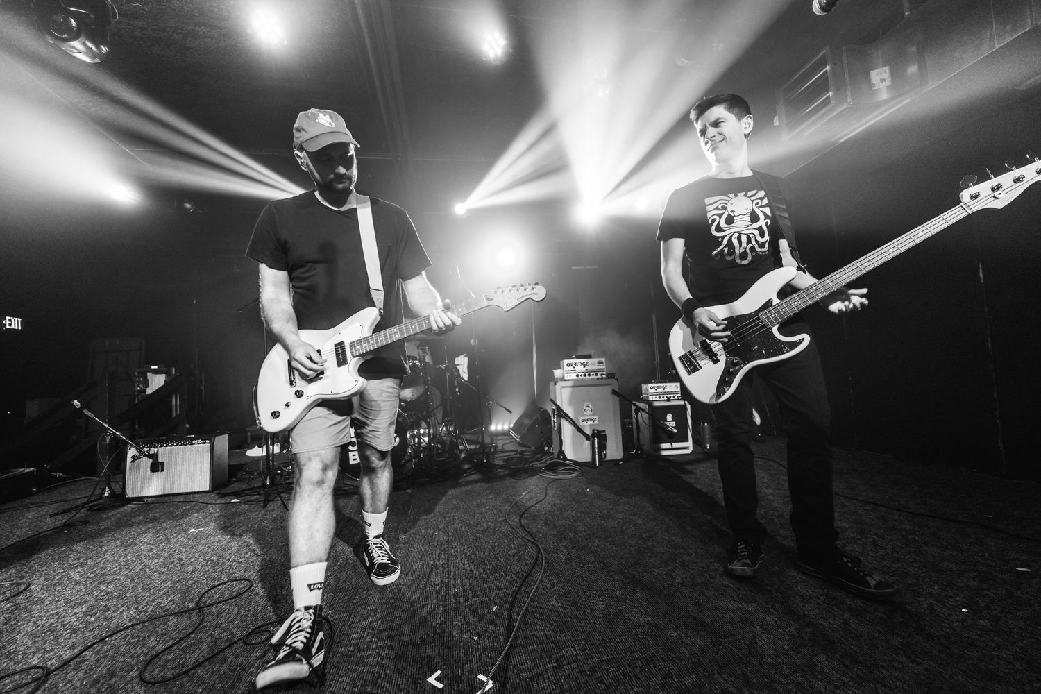 Musicians perform with guitars in black and white under dramatic concert lighting.