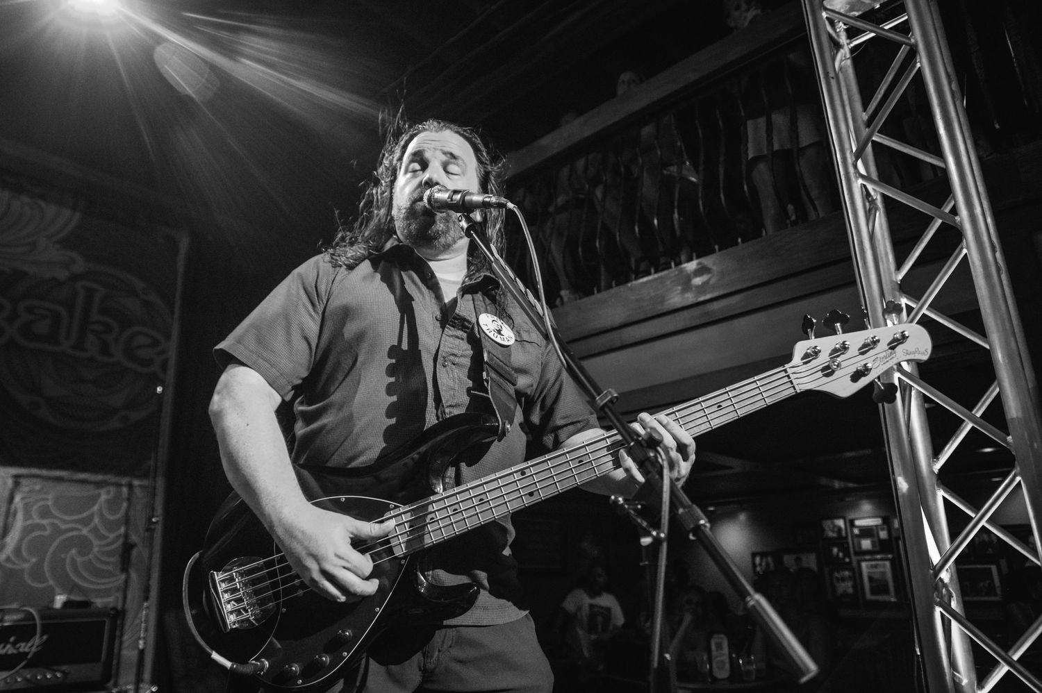 A black and white photo of a bass player performing on stage under dramatic lighting.