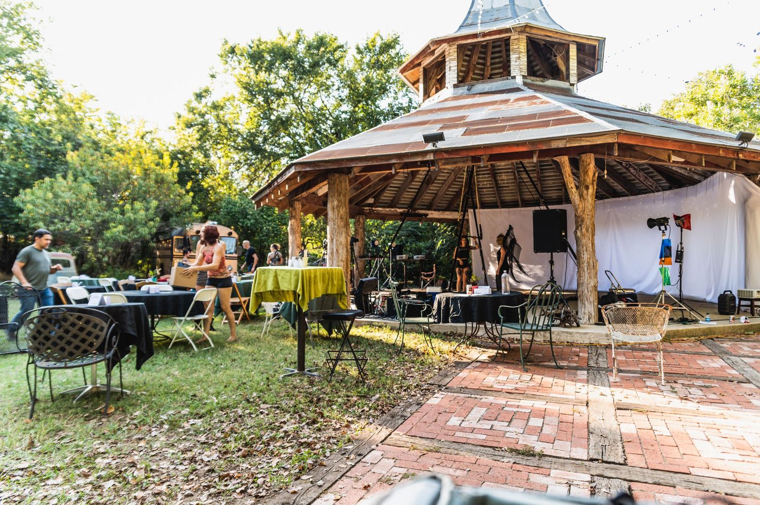 Outdoor gazebo venue with wooden architecture and brick patio surrounded by trees.