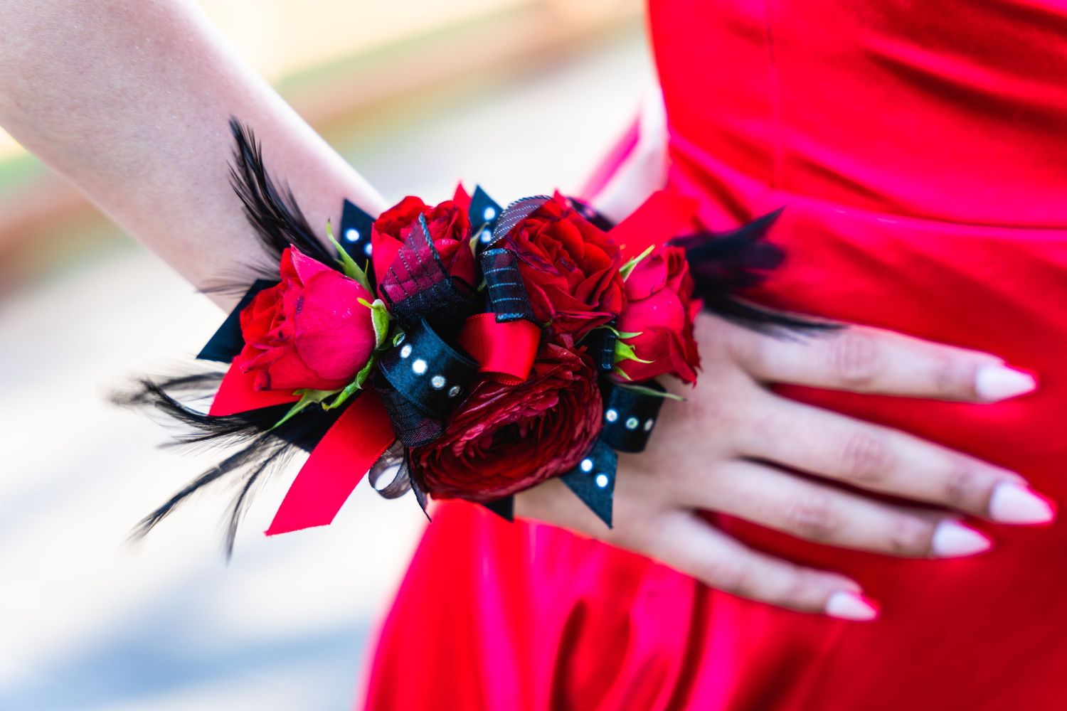 A close-up of a red rose corsage with blue pearls and feather accents worn on a red dress.