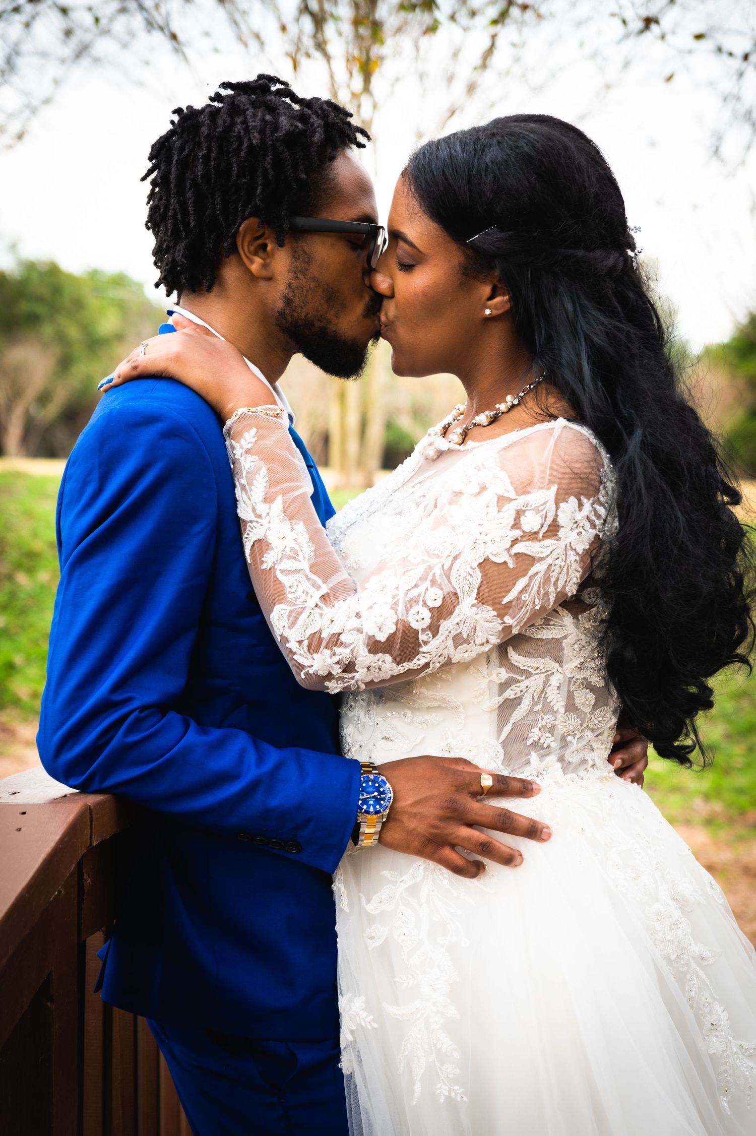 Romantic wedding portrait of couple embracing in white lace dress and royal blue suit on wooden bridge.