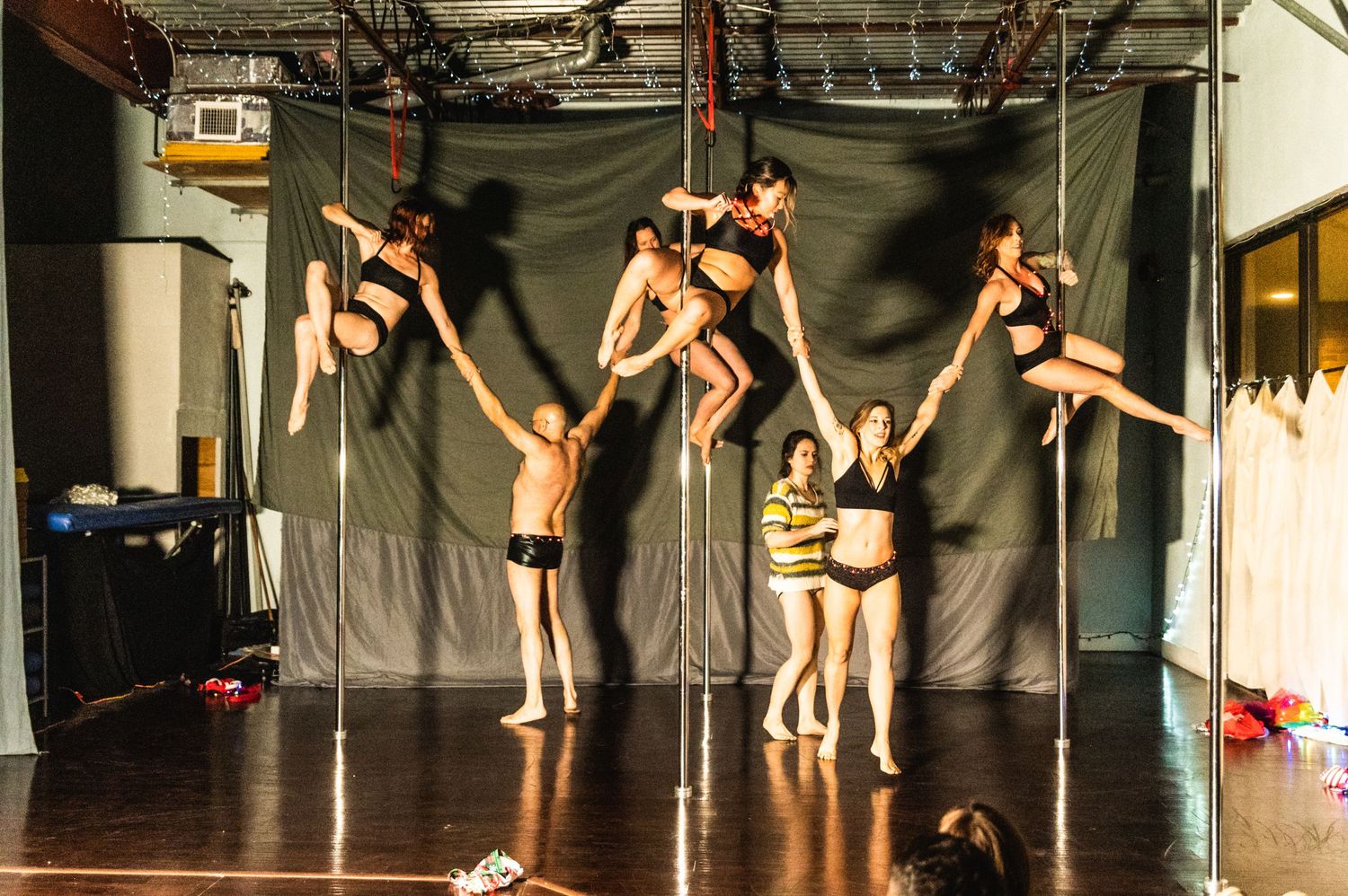 Group of pole dancers perform synchronized routine on multiple poles in studio setting.