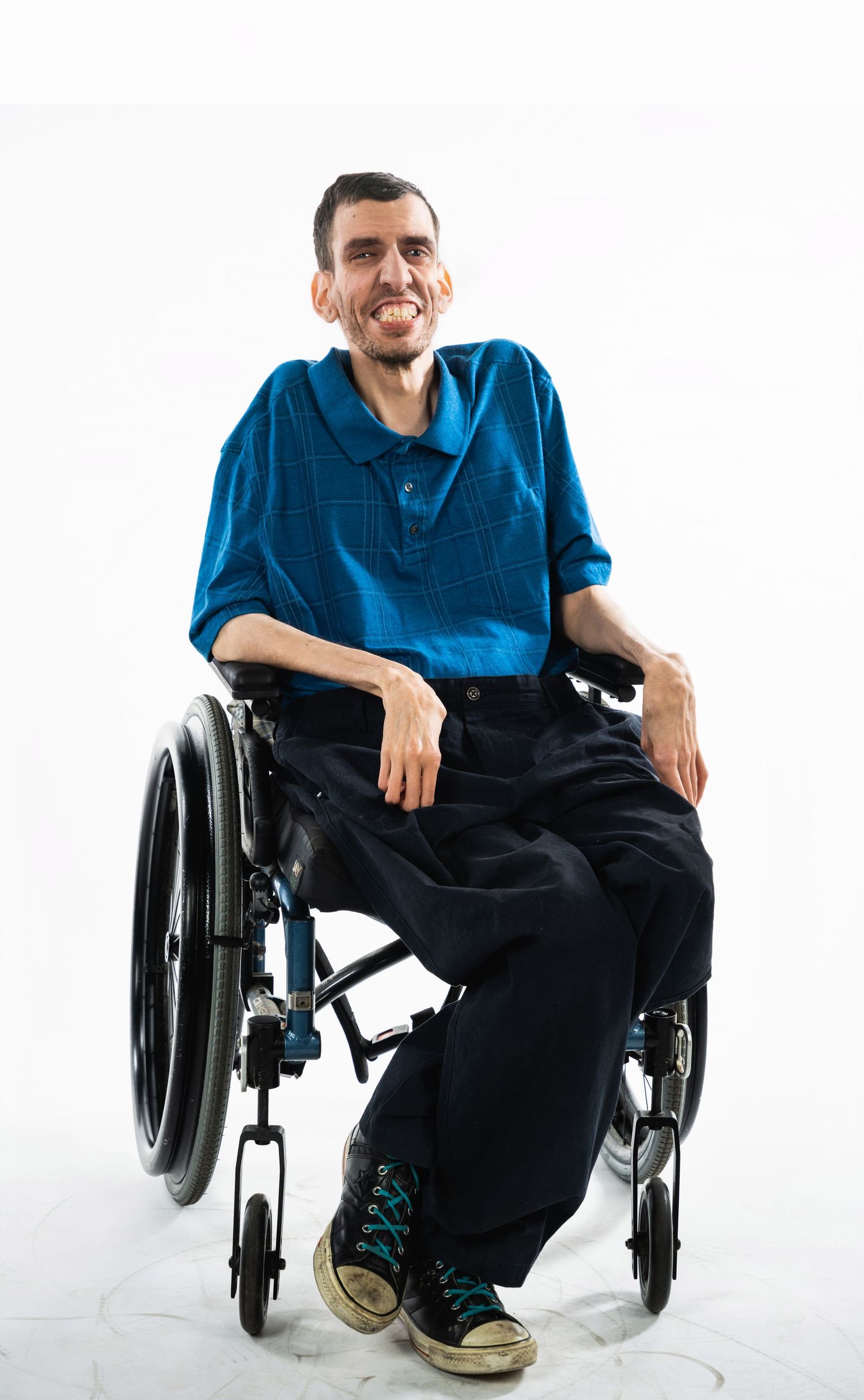 Person wearing blue shirt sitting in wheelchair smiles against white background.