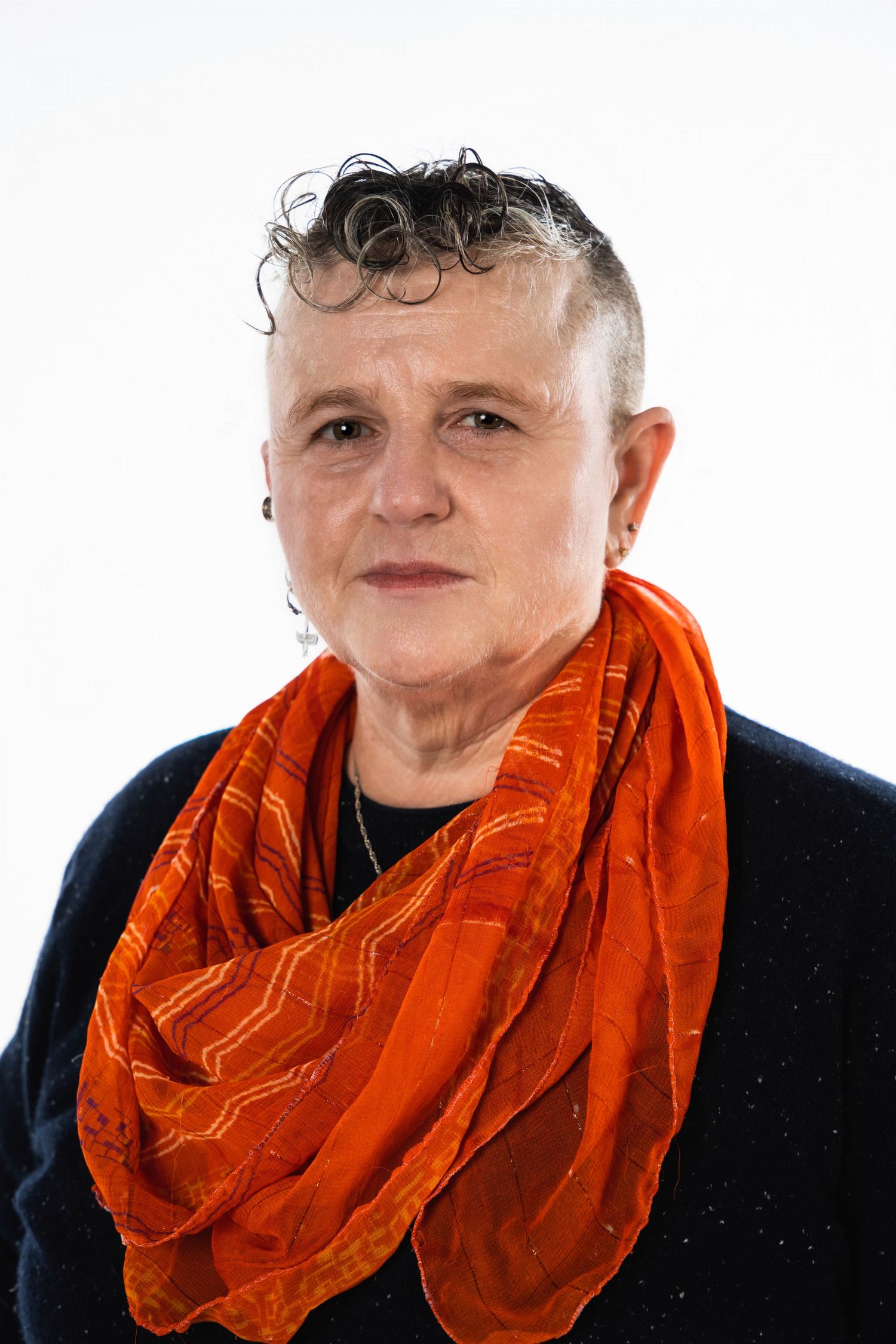 Portrait against white background wearing orange scarf and black top with curly short hairstyle.