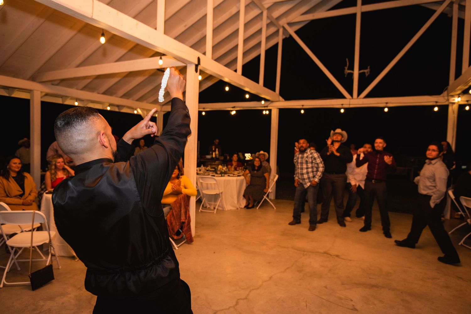 Guest capturing photos during wedding reception in rustic barn with string lights.