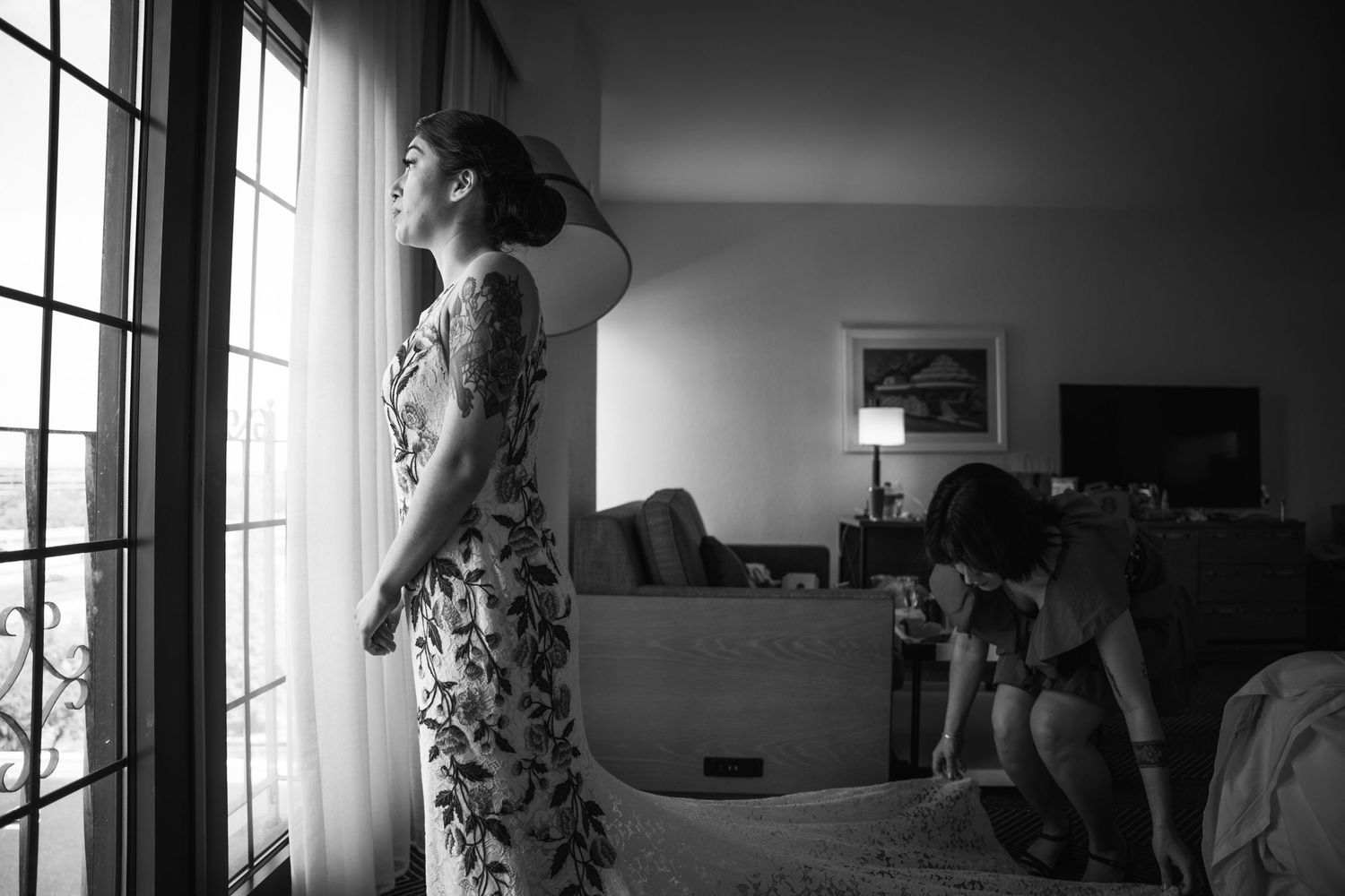 A silhouette stands by a window in a floral dress creating a dramatic black and white composition.