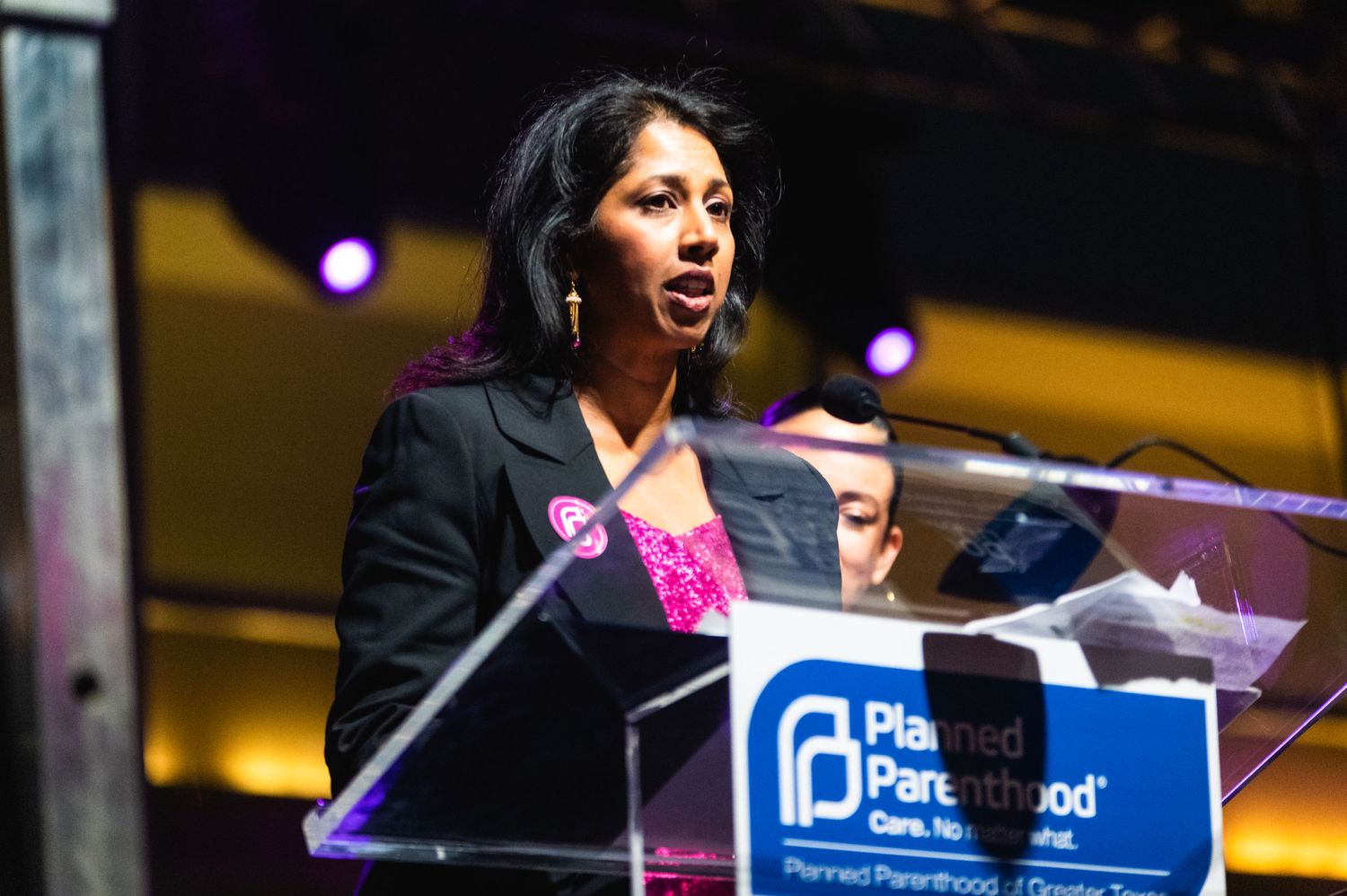 Speaker at a podium with Parenthood logo delivers remarks during an event with purple lighting.