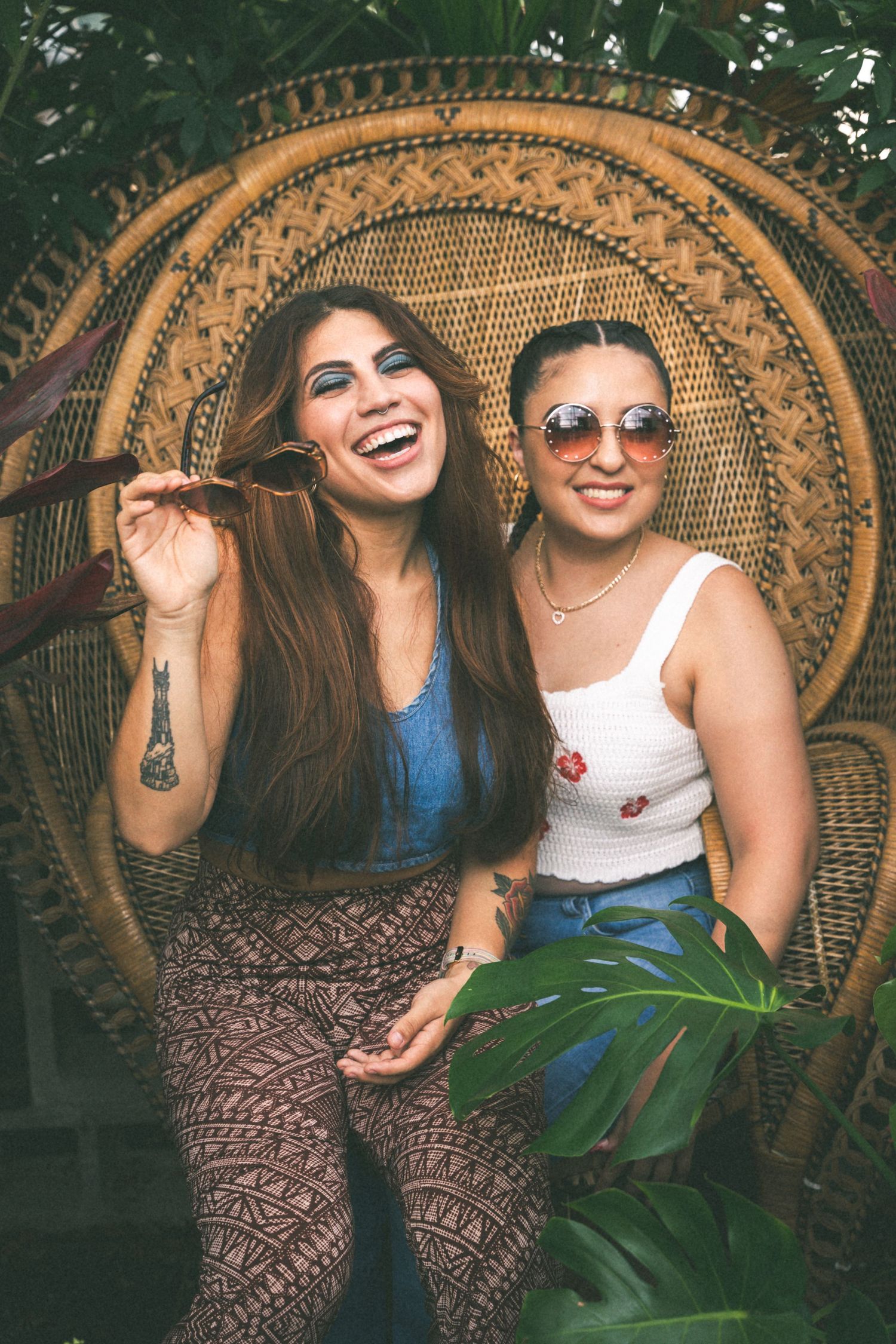 Two friends sitting in a peacock chair surrounded by tropical plants.