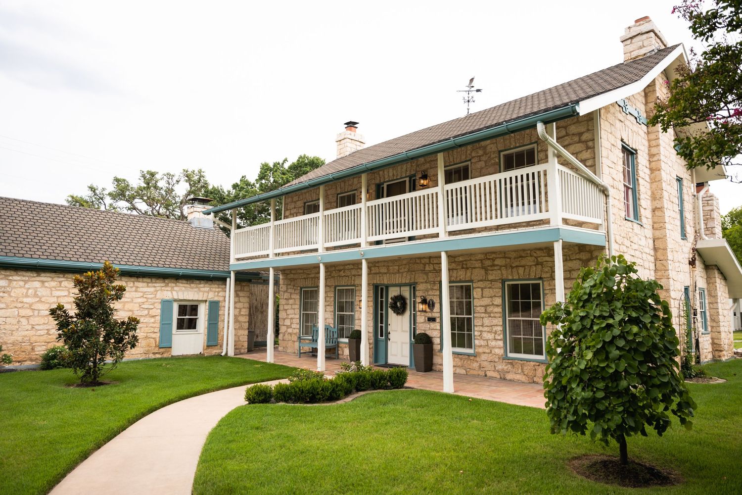 Historic two-story stone building with wraparound porch and well-maintained lawn in Texas.