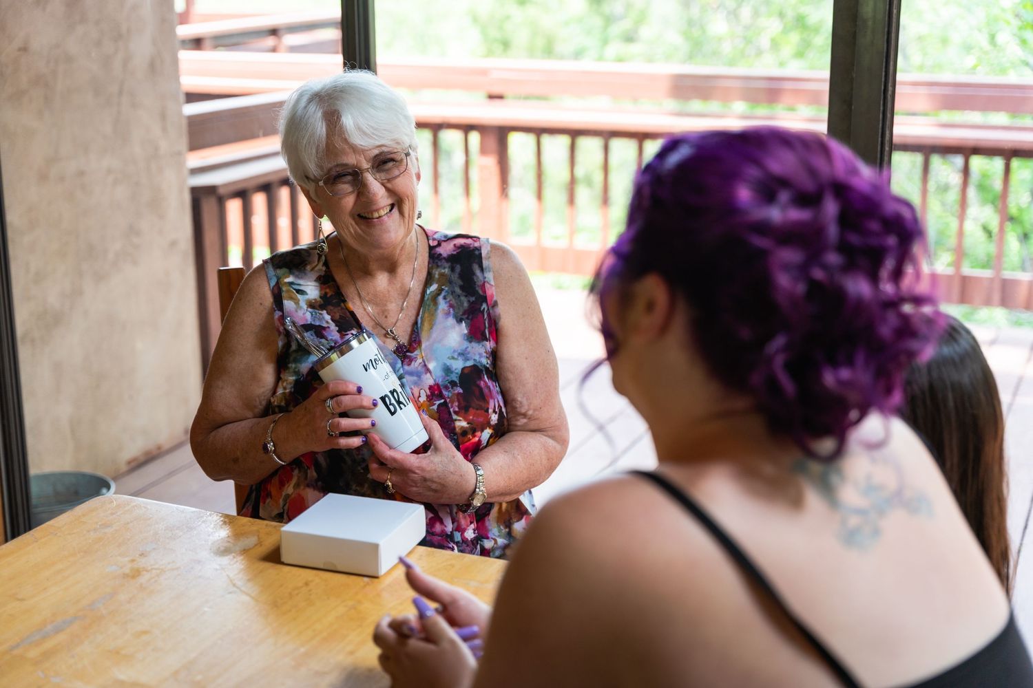 Two people having a discussion at a wooden table on an outdoor porch.