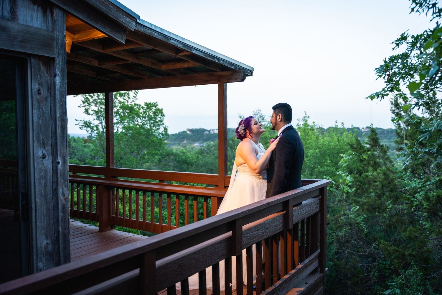 A romantic moment between newlyweds on a rustic cabin deck overlooking a scenic landscape at dusk.