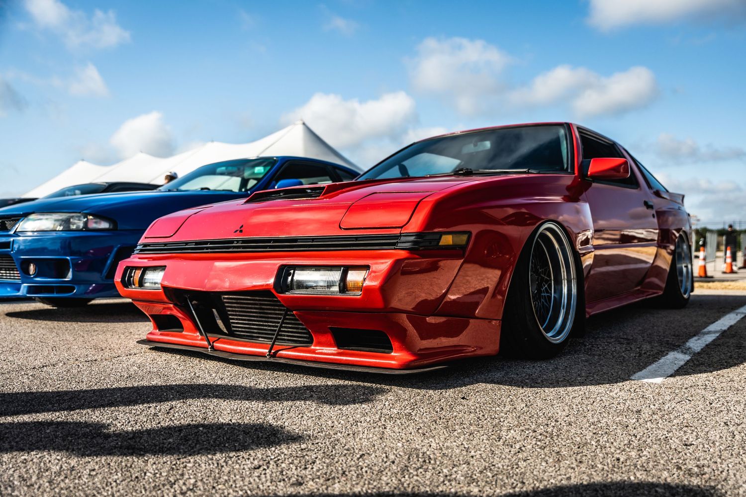 Lowered red Nissan sports car with wide body kit and aggressive styling at car show.