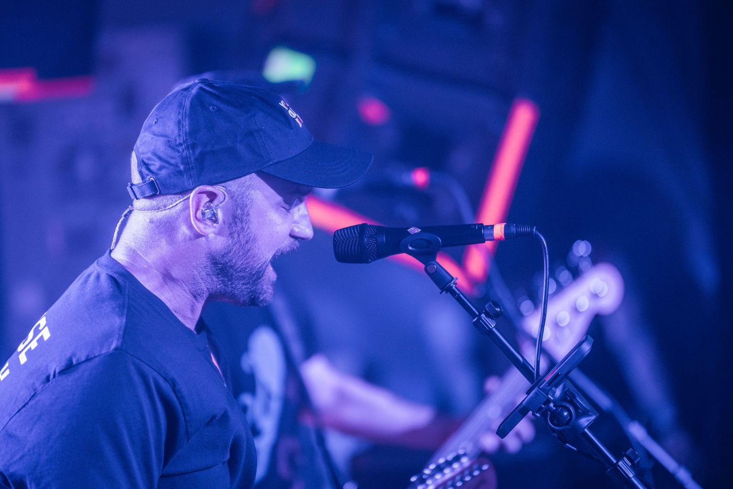 Singer performs at a concert illuminated by blue and red stage lighting while singing into a microphone.