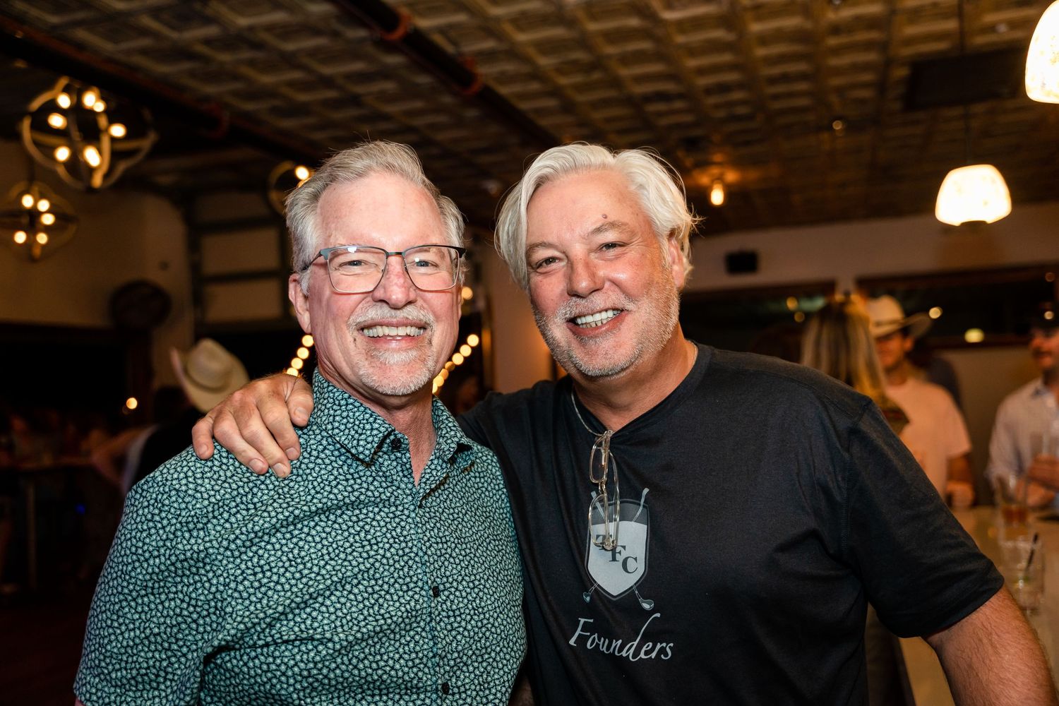 Two friends share a cheerful moment at an indoor venue with warm lighting.