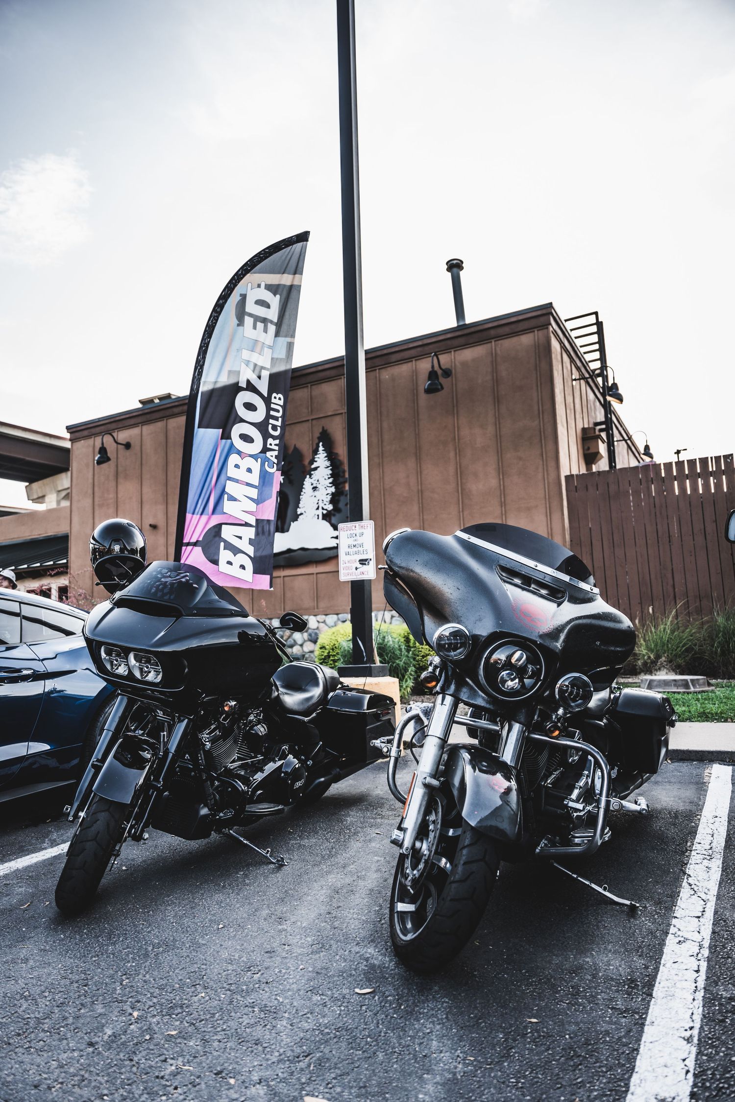 Two black Harley-Davidson motorcycles parked in front of a brick building with a feather flag banner.