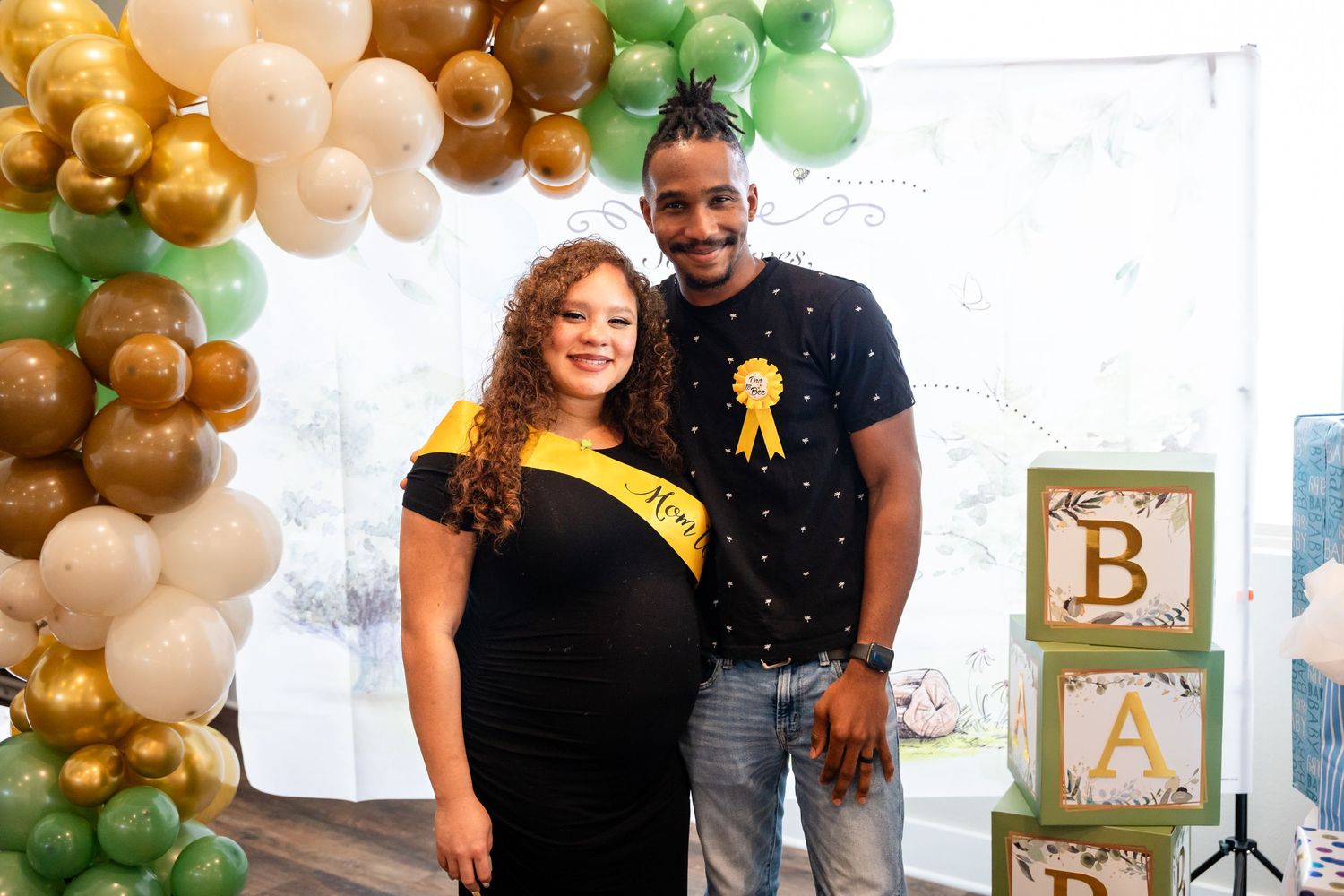 A couple stands together in front of decorative balloon arch and baby blocks at shower celebration.
