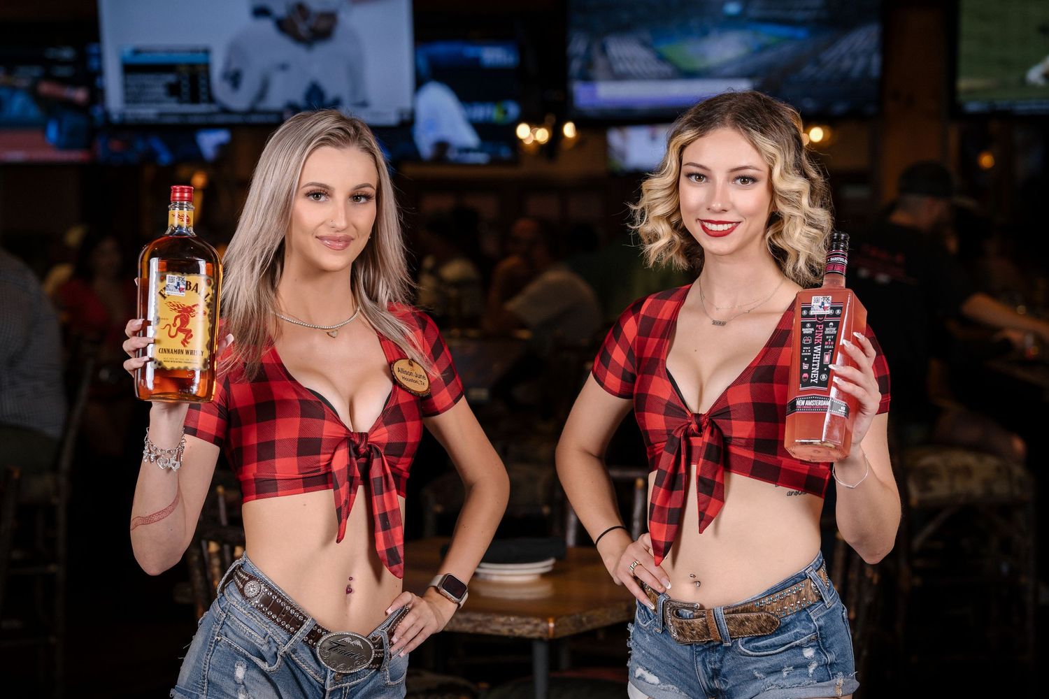 Two servers at sports bar displaying beverages in matching plaid tied tops.