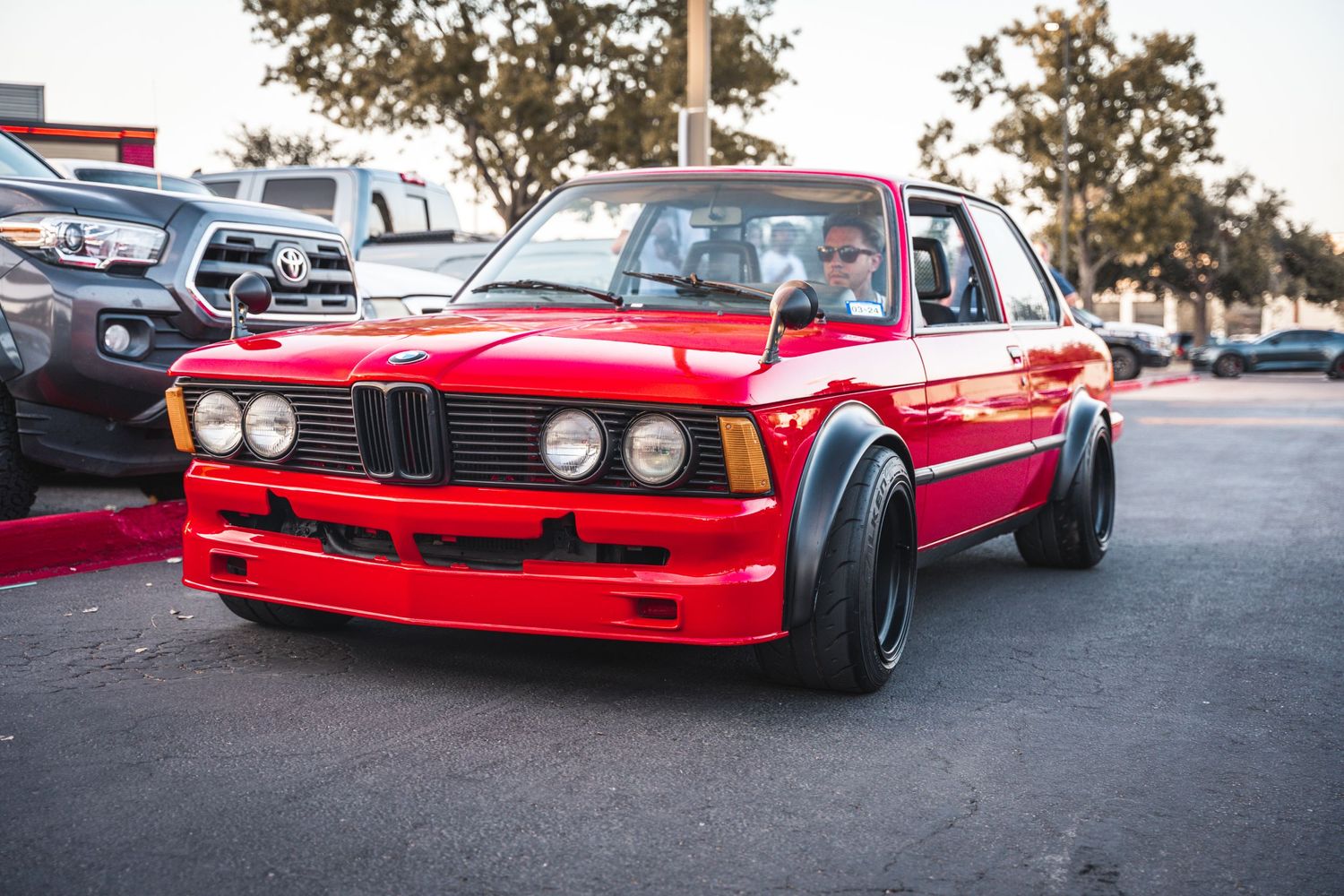 Classic red BMW E30 with widebody kit and custom wheels.
