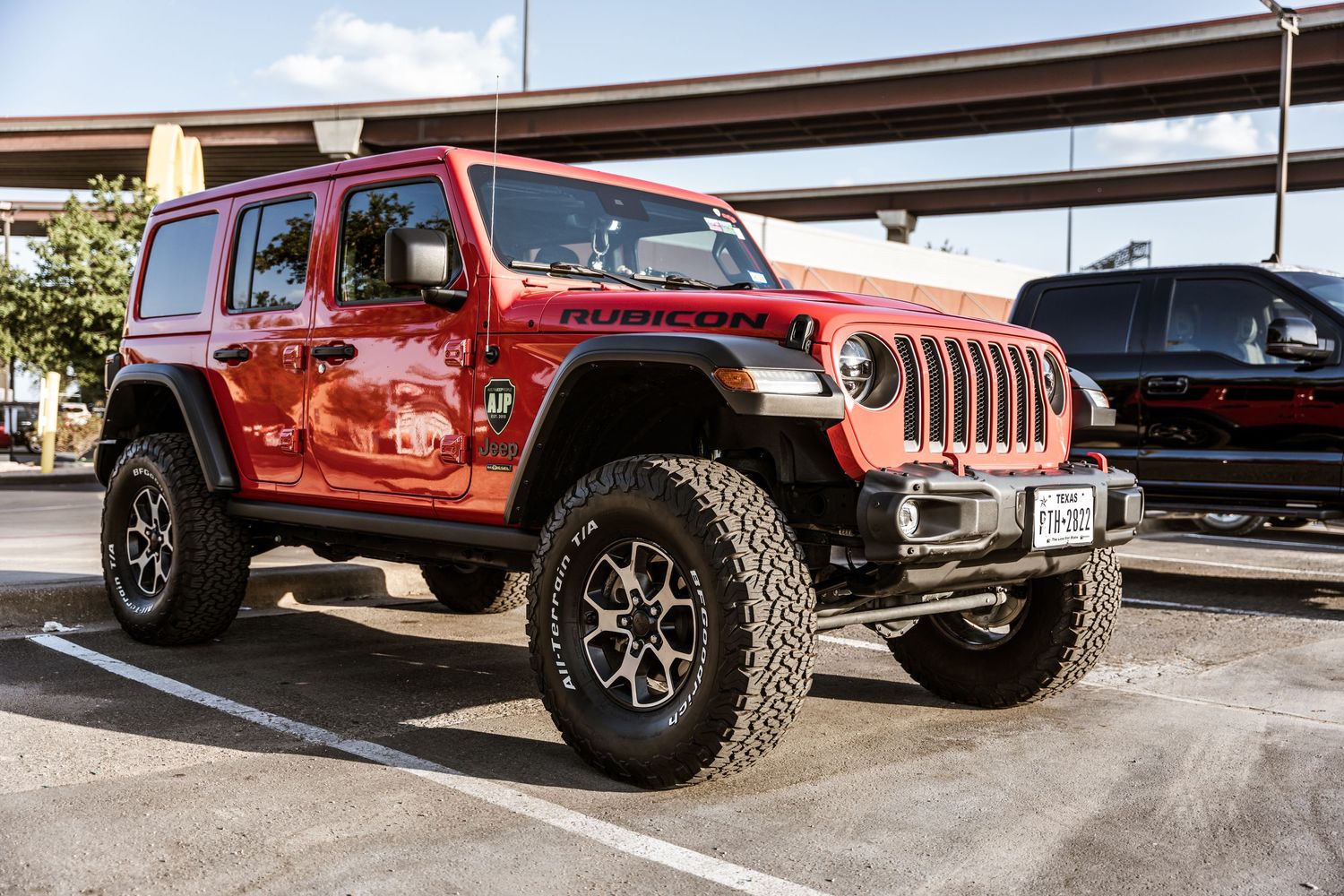 Red Jeep Wrangler with lifted suspension and off-road tires in a parking lot.