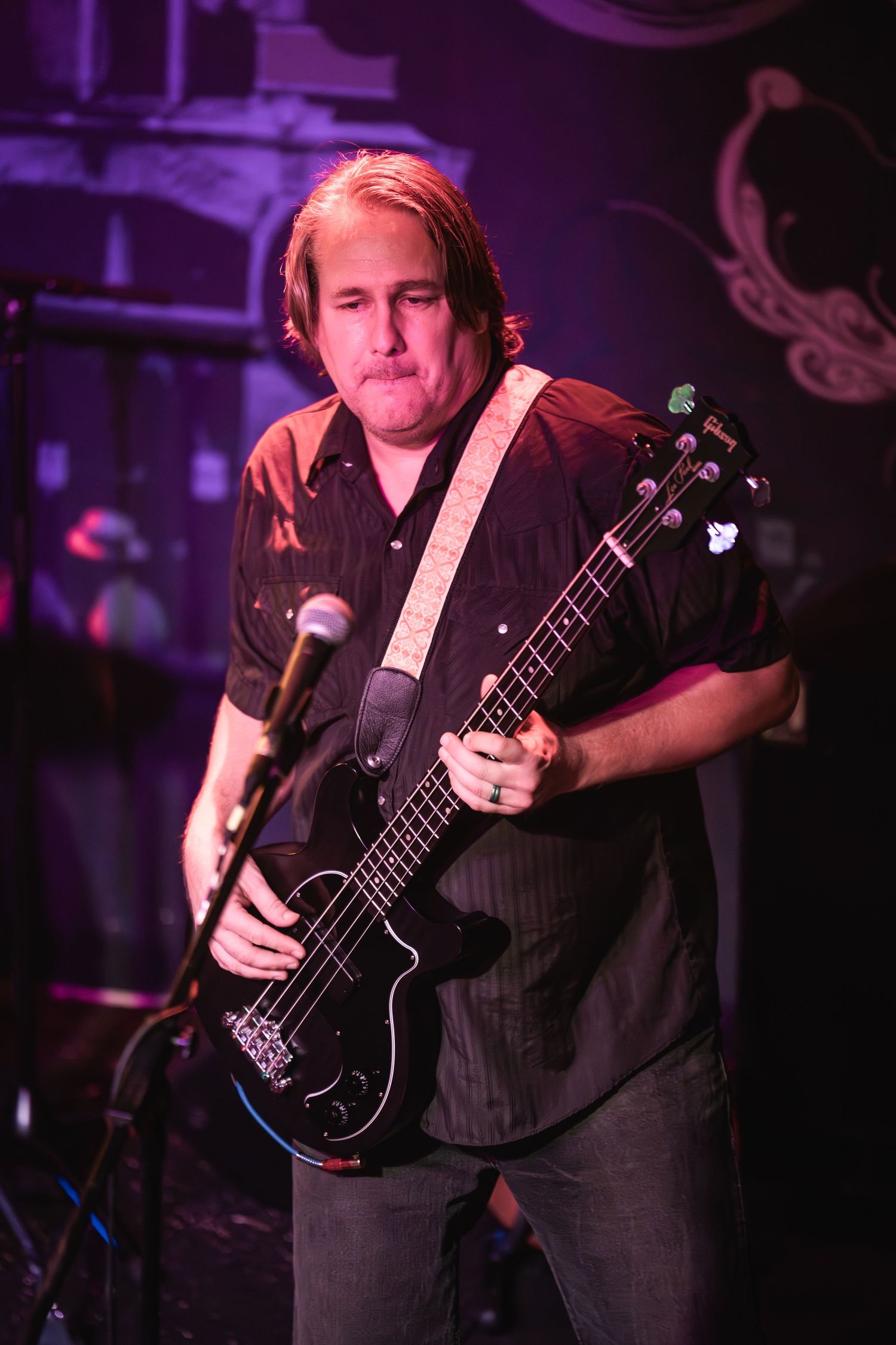 Bass guitarist performs solo under purple stage lighting at intimate venue.
