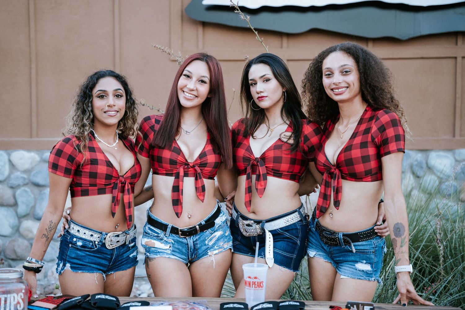 Group wearing matching red plaid crop tops and denim shorts at an outdoor event.