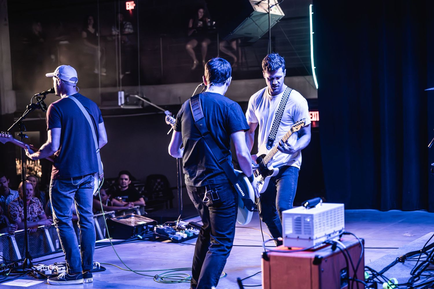 Musicians playing guitars on stage bathed in blue concert lighting.