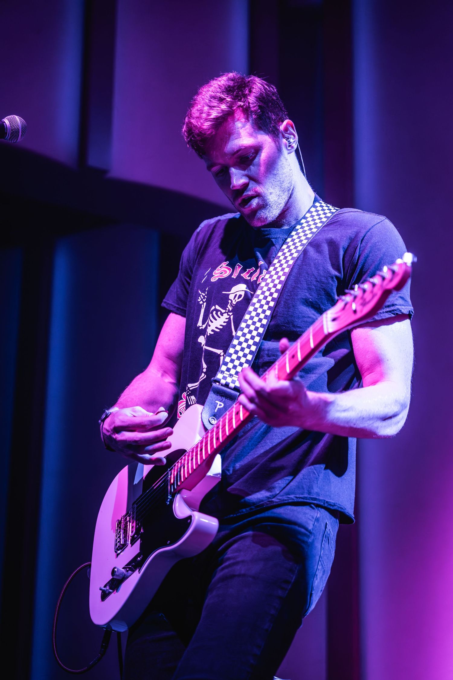 Guitarist performs on stage bathed in purple lighting while playing an electric guitar.