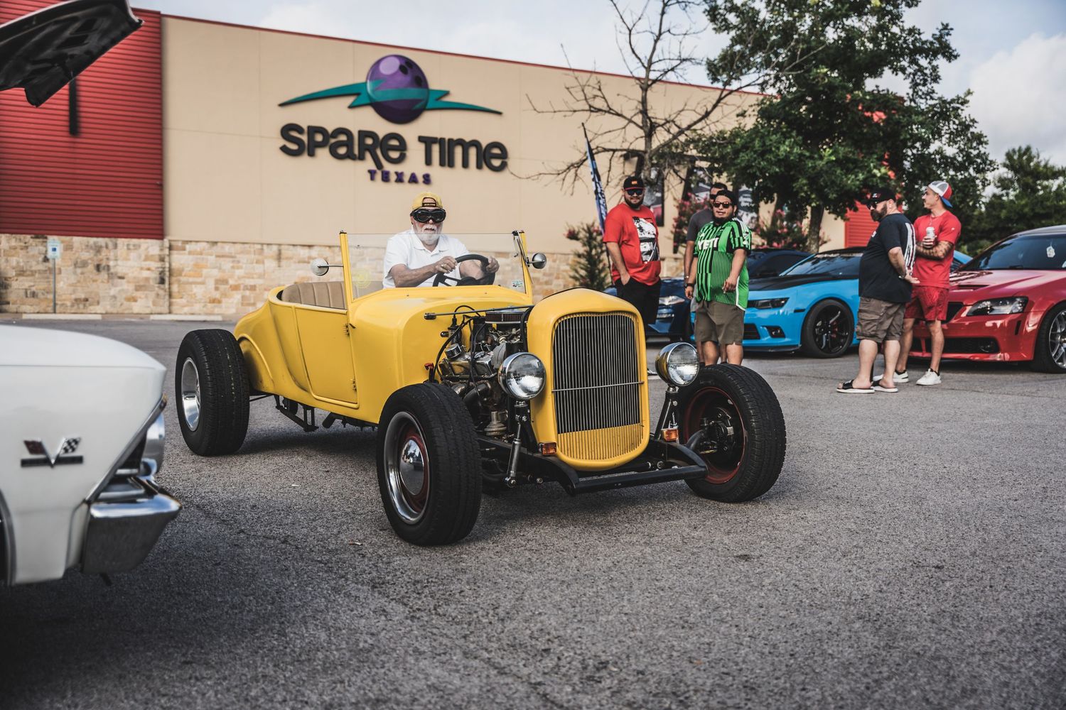Yellow hot rod roadster parked outside retail store at car meet.