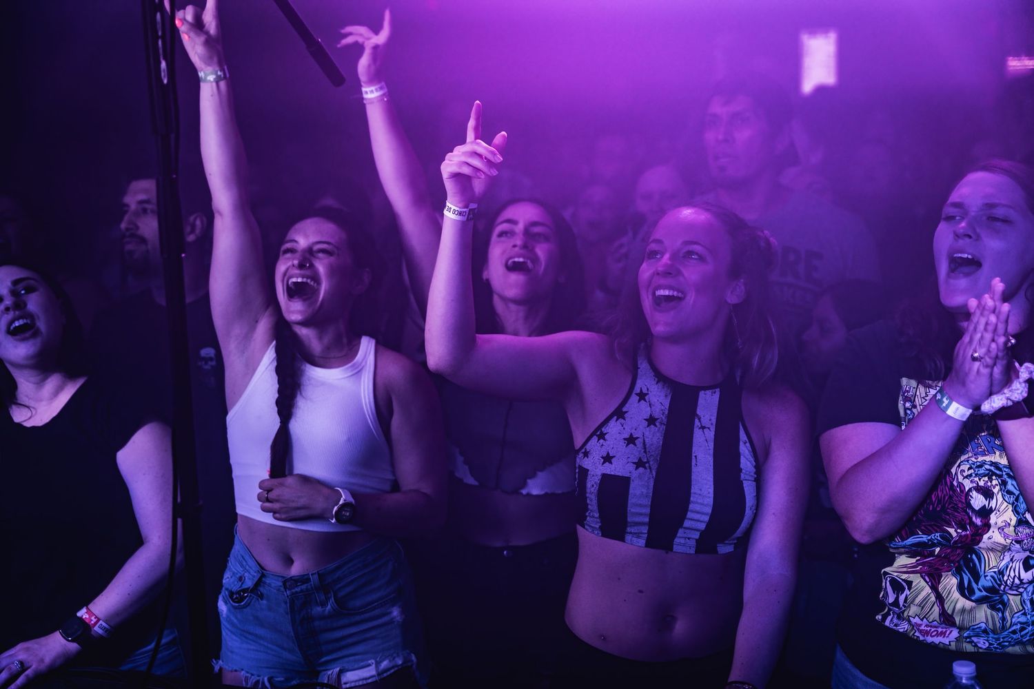 Enthusiastic crowd watching concert under purple lighting.