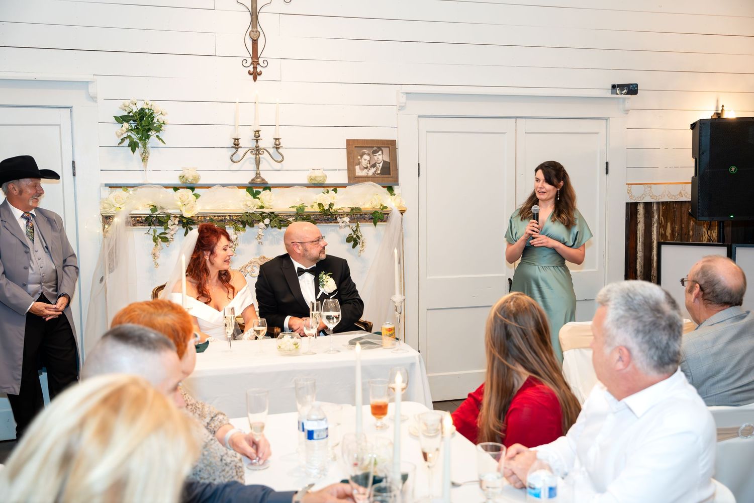 Wedding reception scene with guests seated at tables while someone gives a toast.
